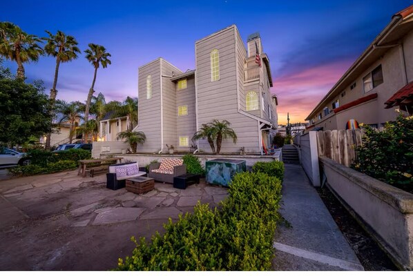 A two-story building with a stone patio, outdoor seating, and palm trees. - Pacific Beach Gem - Steps from Bay & Beach - AC - Fireplace - Paddleboard (San Diego)