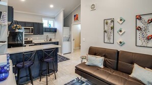 A modern kitchen with dark cabinets, a central island with bar stools, and a brown leather sofa in the living area. - Bring Your Boat! Lake Murray Home w/ Dock & Ramp (Prosperity)