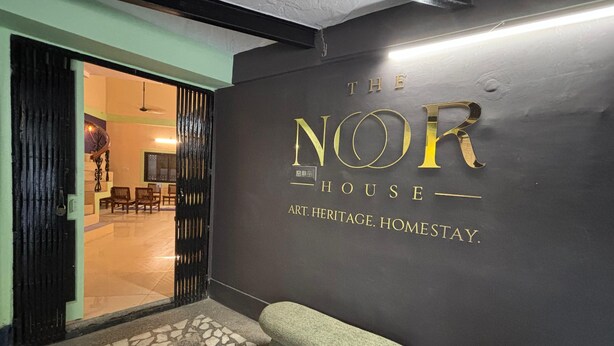 Eine schwarze Wand mit goldener Schrift, auf der 'The NOR House Art Heritage Homestay' steht.