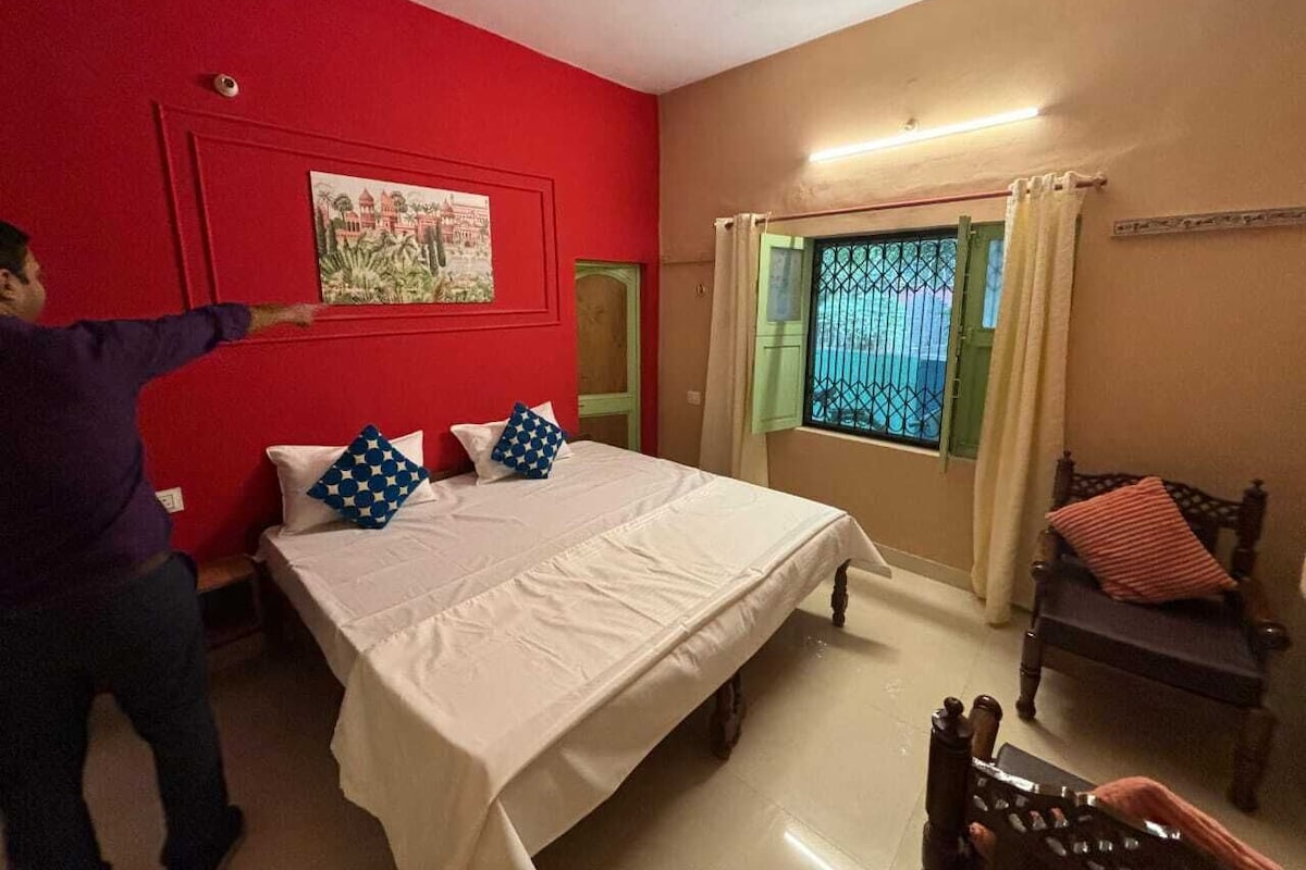 A bedroom with a bed, a window with curtains, a chair, and a painting on the wall.
