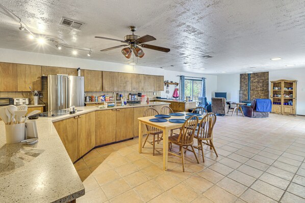 A spacious kitchen with wooden cabinets, a large island, and a dining area with chairs. - Perfect For Groups! Socorro Home Near NM Tech (Socorro)