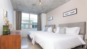 Een hotelkamer met twee bedden, een houten dressoir, een groot raam en uitzicht op een gebouw.