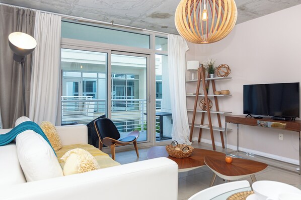 A modern living room with a sofa, chairs, a TV, and a balcony view.