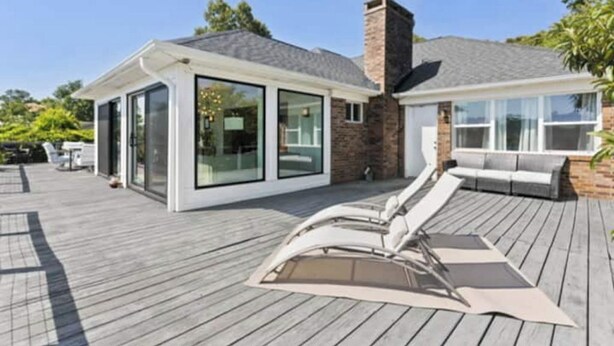 A modern house with a deck, a glass-enclosed room, and a lounge area with outdoor furniture. - Beautiful waterfront house located in Hampstead, NC (Hampstead)