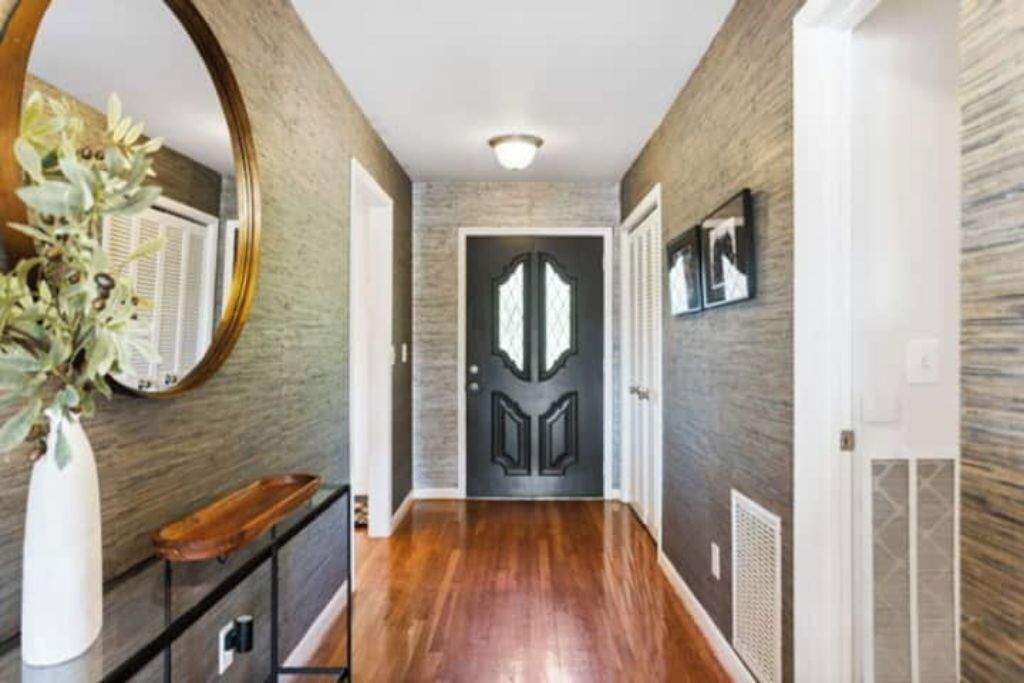 A hallway with a wooden floor, a mirror, a door with a decorative design, and a wall-mounted picture frame.