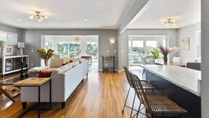 A spacious living area with a wooden floor, a white sofa, a dining table, and a kitchen area with a bar counter. - Beautiful waterfront house located in Hampstead, NC (Hampstead)