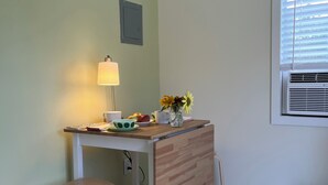 Un petit coin cuisine avec une table en bois, une chaise, une lampe et une fenêtre avec des stores.