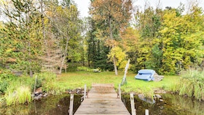 Eine Holzstege führt zu einem Teich, der von Bäumen mit Herbstlaub umgeben ist.