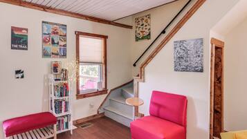A cozy room with a red chair, a bookshelf, a bench, and a staircase with a wooden railing.
