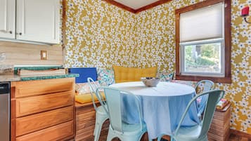 Un coin repas avec une table ronde, des chaises bleues et un banc jaune avec coussin.