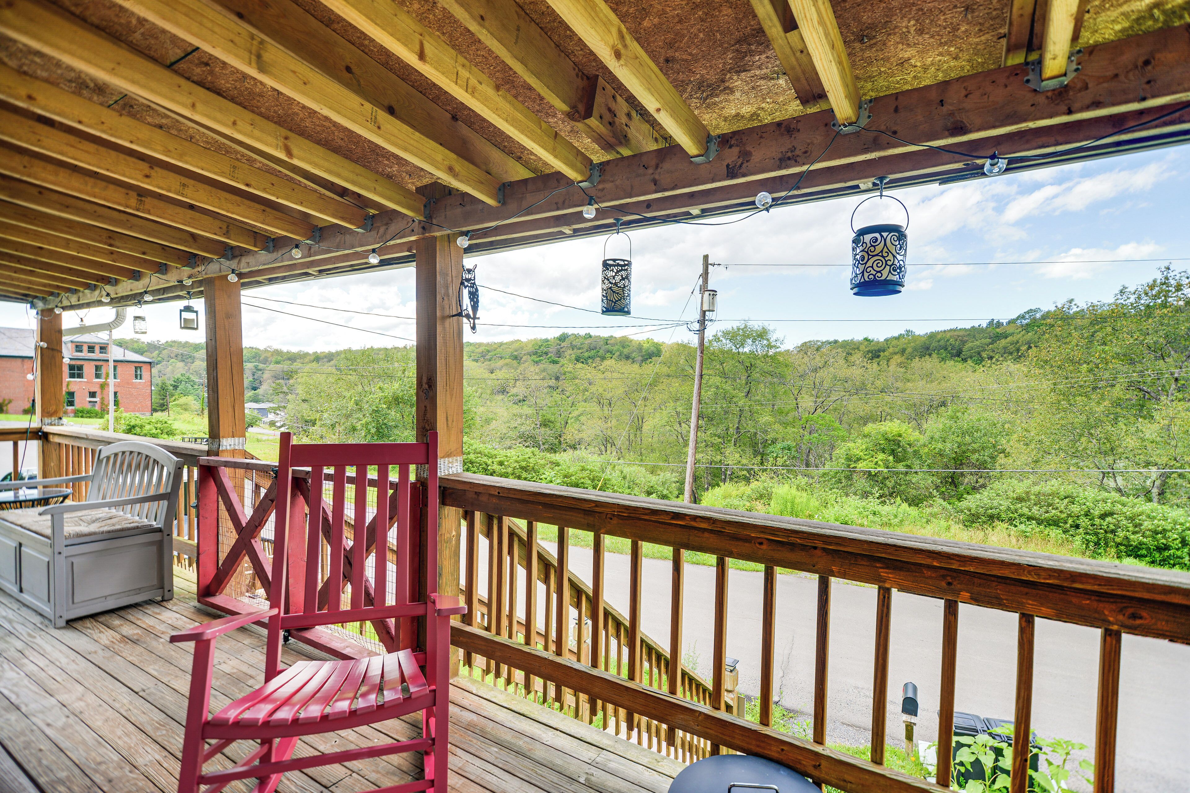 A wooden deck with a red chair, a barbecue grill, and a view of a green landscape.