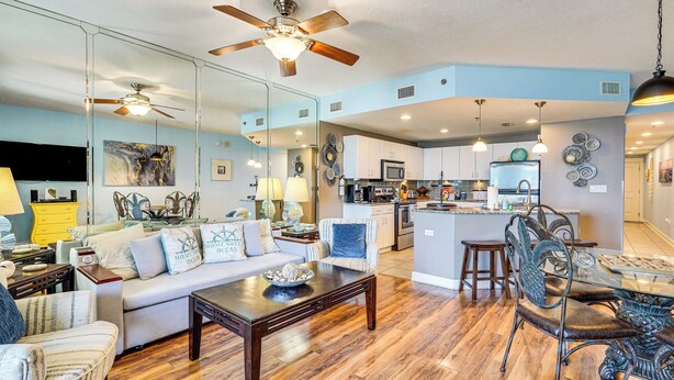 A spacious living room with a sofa, coffee table, and decorative items. A kitchen with modern appliances is visible in the background.