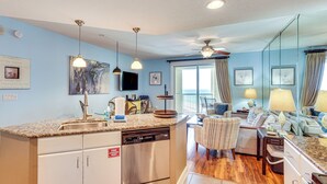 A modern kitchen with a dishwasher, a dining area with a sofa and a table, and a living room with a TV and artwork on the walls.