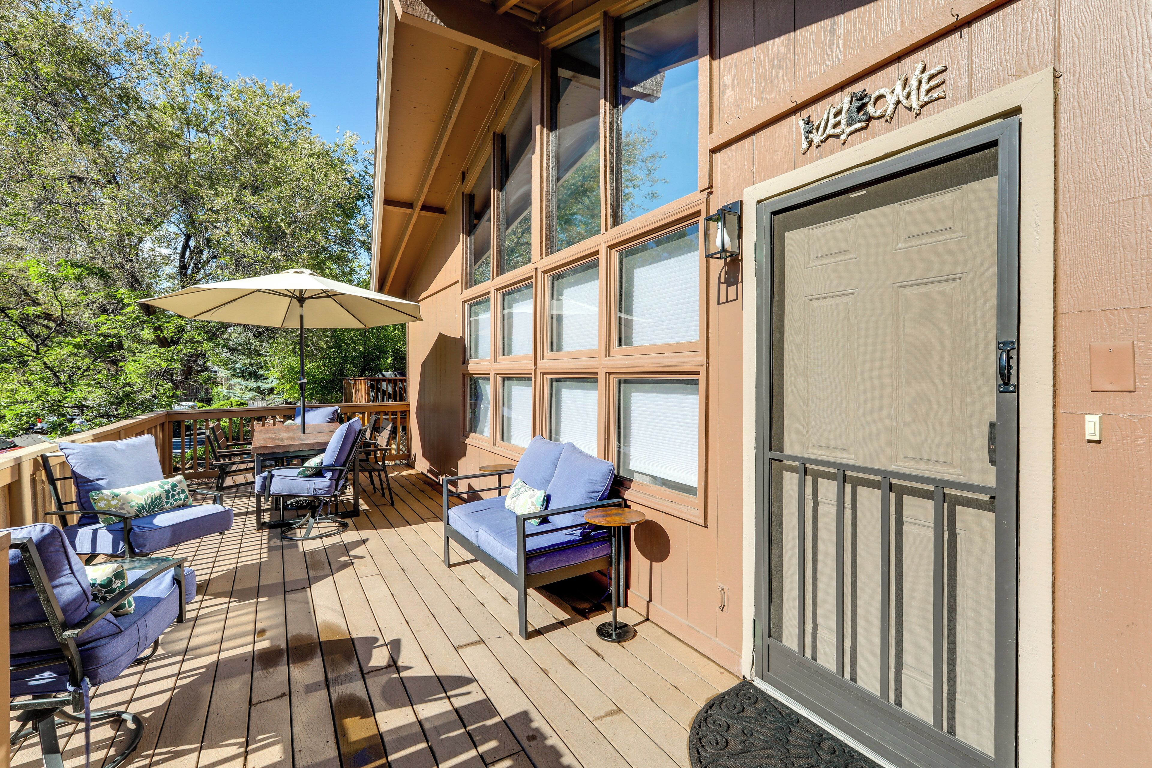 Una terraza de madera con mobiliario exterior, una zona cubierta y un amplio ventanal corredizo con un letrero de bienvenida.