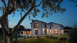Una casa moderna de dos pisos con un césped cuidado y un árbol grande al frente.