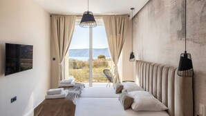 A bedroom with a large bed, two bedside lamps, a view of the outdoors, and a mounted TV. - Villa Neoma – Tranquil Seaside Escape with Heated Pool and Breathtaking Sea Views (Linardići (Krk))