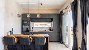 A modern kitchen with a central island, black chairs, and pendant lighting. - Villa Neoma – Tranquil Seaside Escape with Heated Pool and Breathtaking Sea Views (Linardići (Krk))