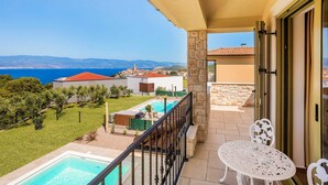 A balcony with a pool, a table, and a view of the sea and buildings. - Villa Pinaza B – Romantic Seaside Retreat with Heated Pool, Sauna, and Jacuzzi in Vrbnik (Vrbnik (Krk))