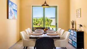 Uma sala de jantar com mesa posta para seis pessoas, vista para o verde e montanhas através de uma porta de vidro, e um abajur decorativo sobre a mesa.