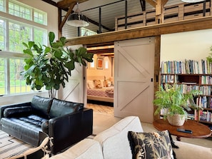 A spacious living area with a black leather sofa, a light-colored sofa, a large potted plant, and a wooden bookshelf filled with books. - Hill Ross Stables Historic Homestead (Northampton)