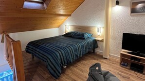 Una camera da letto con soffitto spiovente, un letto con copripiumino a righe, una televisione e una poltrona sacco.