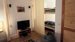 Una stanza con televisione su un supporto in legno, un letto a castello e due sacchi di fagioli.