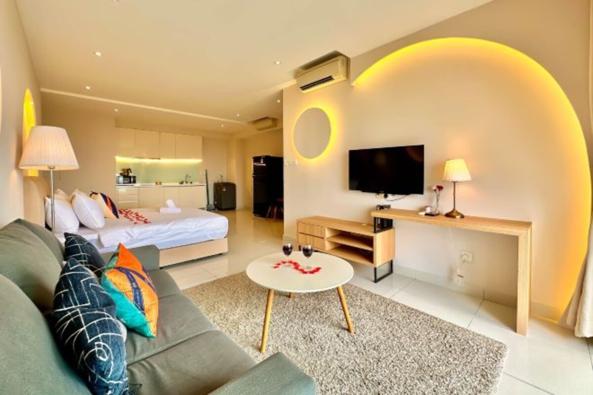 Quarto de hotel moderno com sofá, mesa de centro redonda, cama, televisão e cozinha.