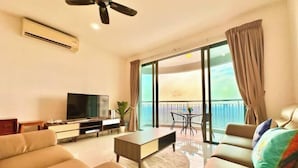 A modern living room with a sofa, a coffee table, a TV, and a balcony with a view. - Teega Suites by RR JBcity (Iskandar Puteri)