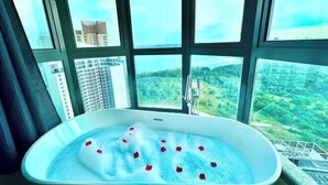A bathtub with rose petals, large windows, and a view of a cityscape. - Teega Suites by RR JBcity (Iskandar Puteri)