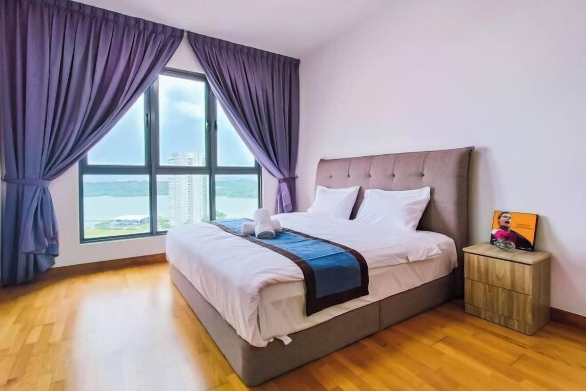 Una camera da letto con un letto grande, un comodino, una finestra con tende e vista sugli edifici.