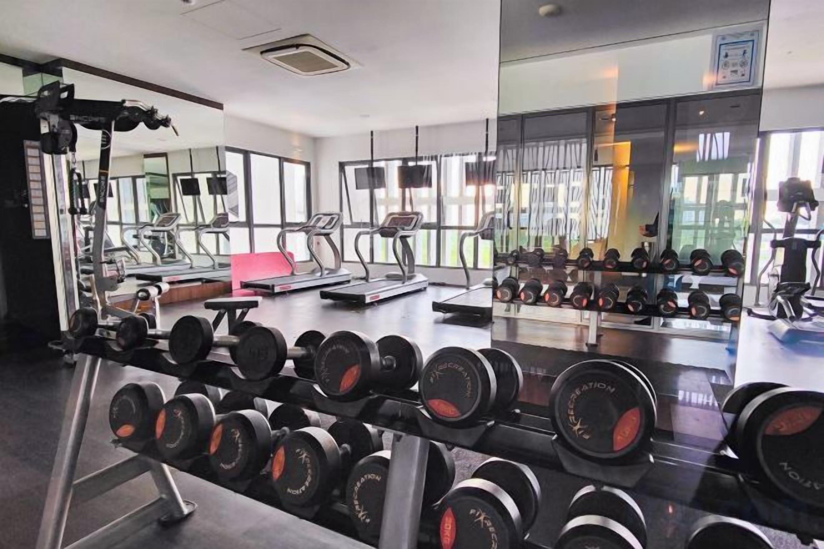 Une salle de sport équipée de machines d’exercice, de supports pour les poids, de tapis de course et d’un mur recouvert de miroirs.