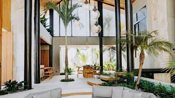 A spacious indoor area with a modern design, featuring a large seating area with a sofa and a round table, surrounded by plants and a small water feature. - Award-Winning 3BR Villa 25m Pool Villa FEH (Bali)