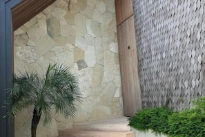 Un muro di pietra con una trama decorativa, una palma e un siepe verde.