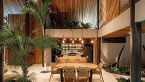 A modern dining area with a round table and chairs, surrounded by plants and a wooden ceiling. - Award-Winning 3BR Villa 25m Pool Villa FEH (Bali)