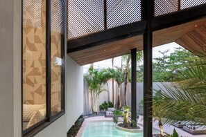 A modern indoor pool area with a view of the outdoors, including palm trees and a seating area. - Award-Winning 3BR Villa 25m Pool Villa FEH (Bali)