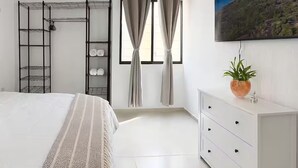 Ein Schlafzimmer mit Bett, Kleiderschrank, einer eingebauten Schrankwand, einem Fernseher und einem Fenster mit Vorhängen.