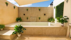 Ein moderner Außen-Wellnessbereich mit Whirlpool, Blumentöpfen und Sonnensegel.