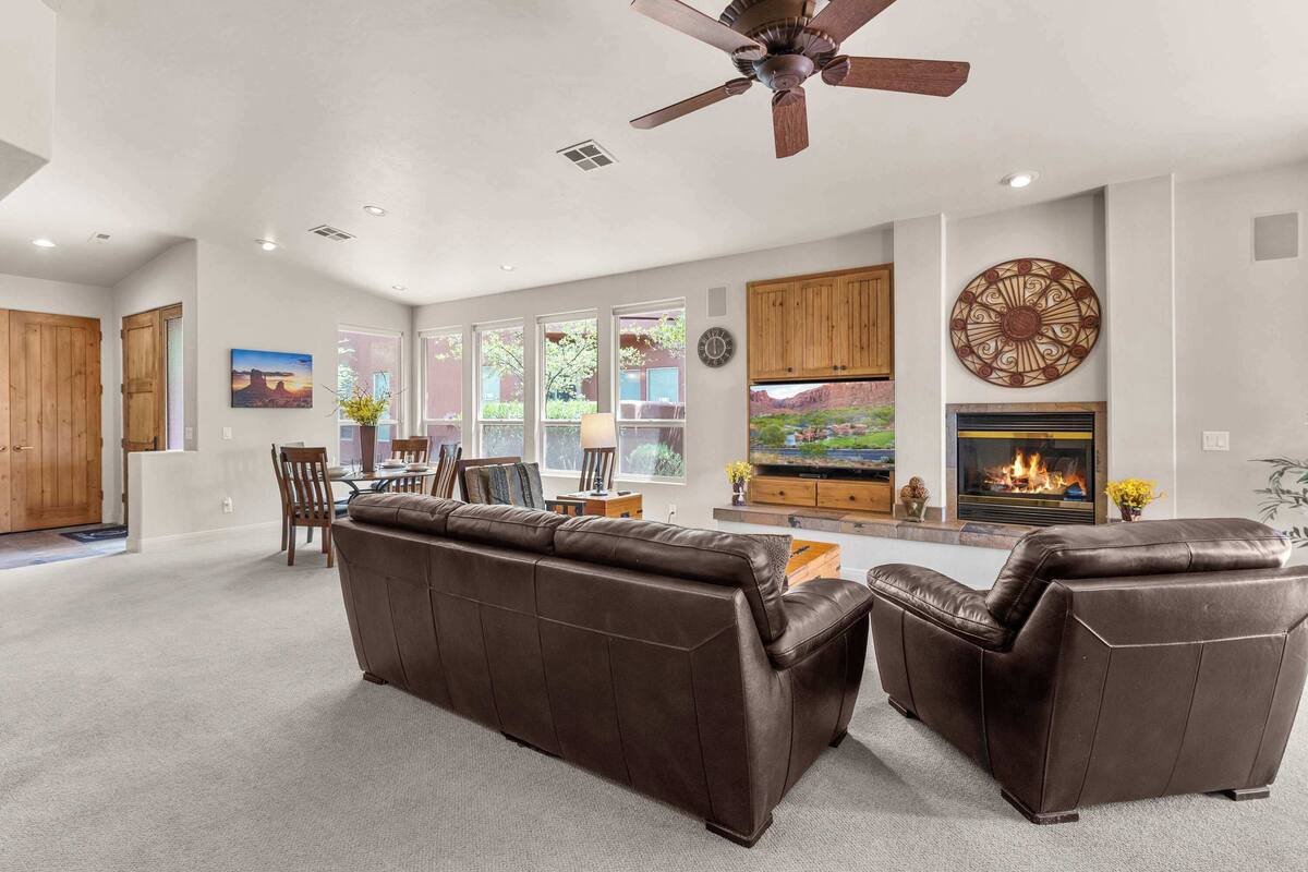 A spacious living room with a brown leather sofa, wooden cabinets, a fireplace, and a ceiling fan.
