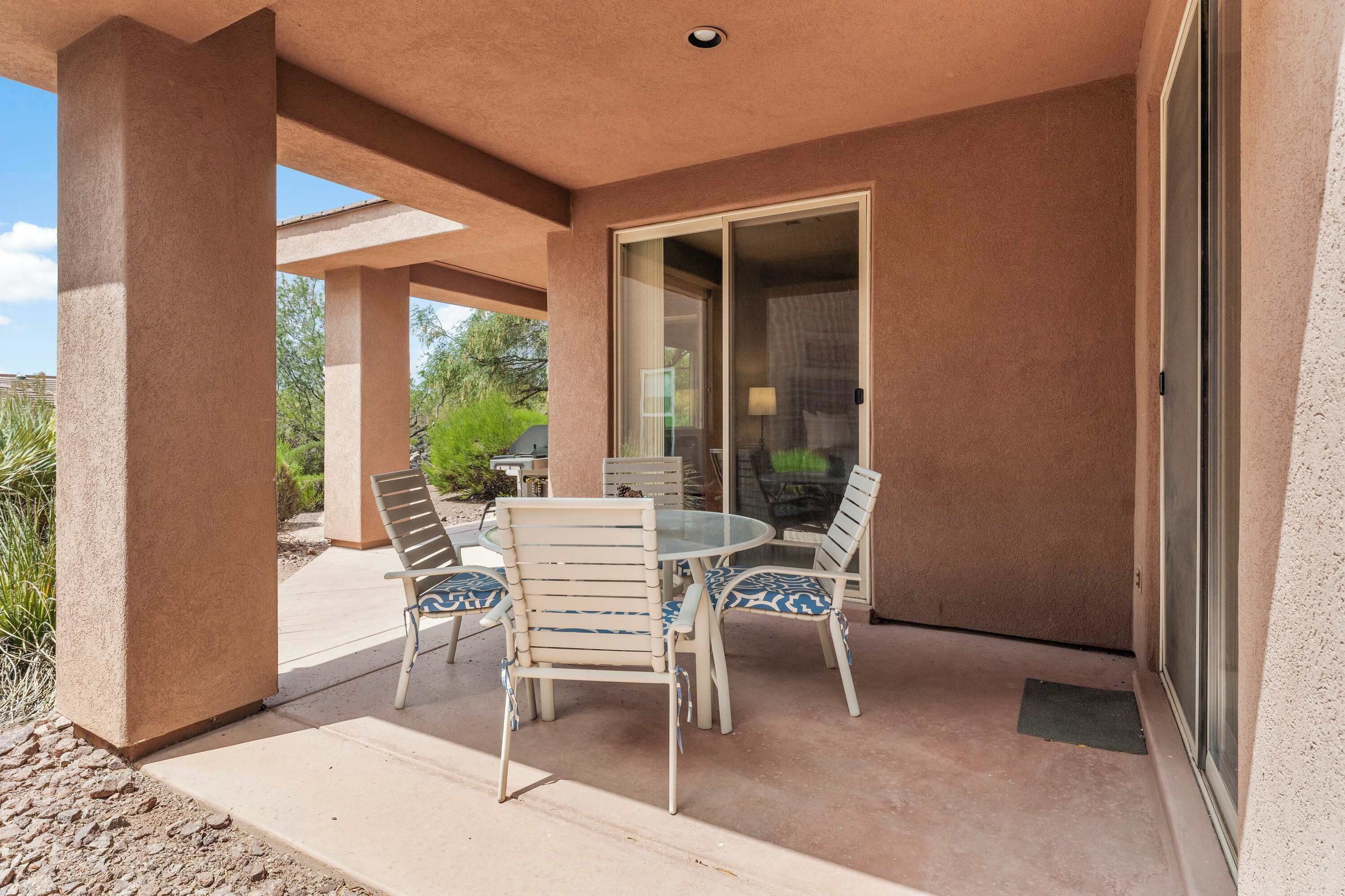 A covered patio with a table and chairs, a sliding glass door, and a view of the outdoors.