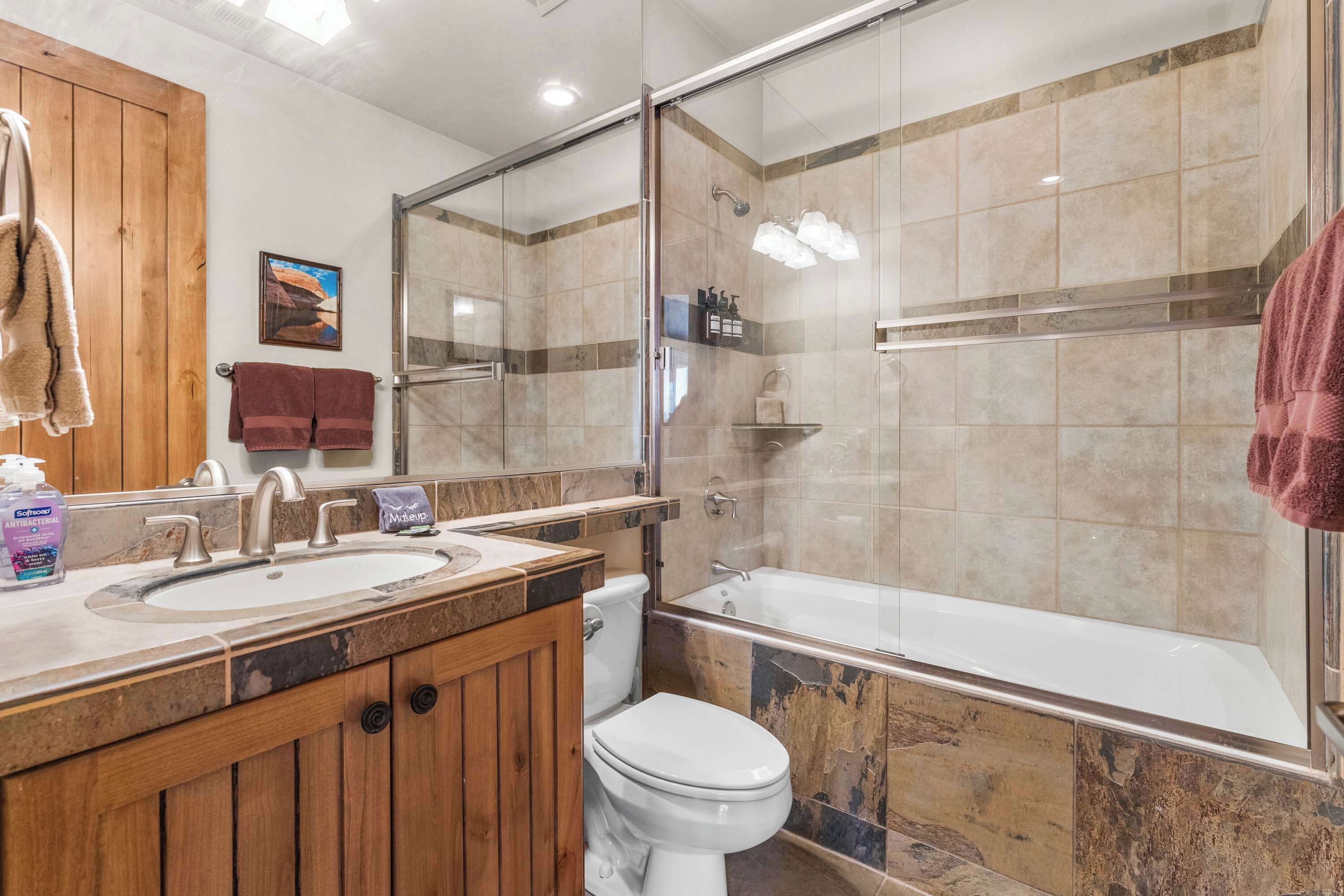 A bathroom with a wooden vanity, a sink, a toilet, and a shower area.