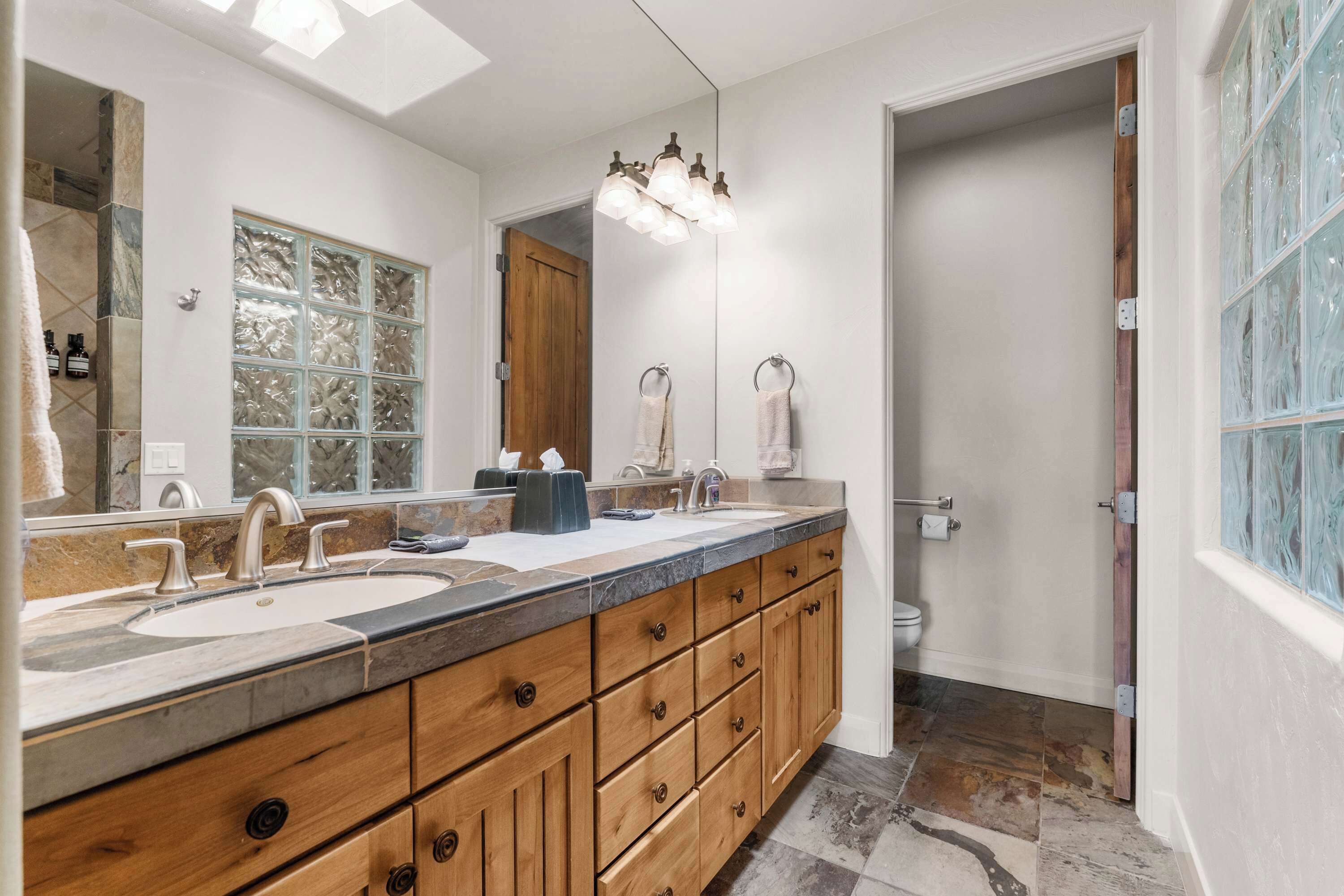 A bathroom with a double sink vanity, wooden cabinetry, a large mirror, and a shower area.