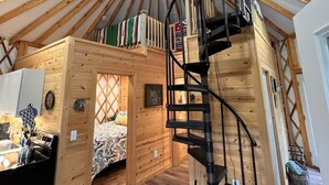 Une yourte avec un intérieur en bois, un escalier en colimaçon et un lit avec une literie à motifs.