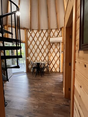 Una habitación con piso de madera, una mesa de comedor con sillas, una escalera espiral negra y una pared con celosía.