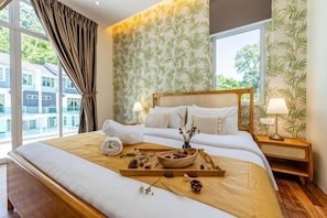 A hotel room with a large bed, a wooden nightstand, a window with curtains, and a view of buildings outside.