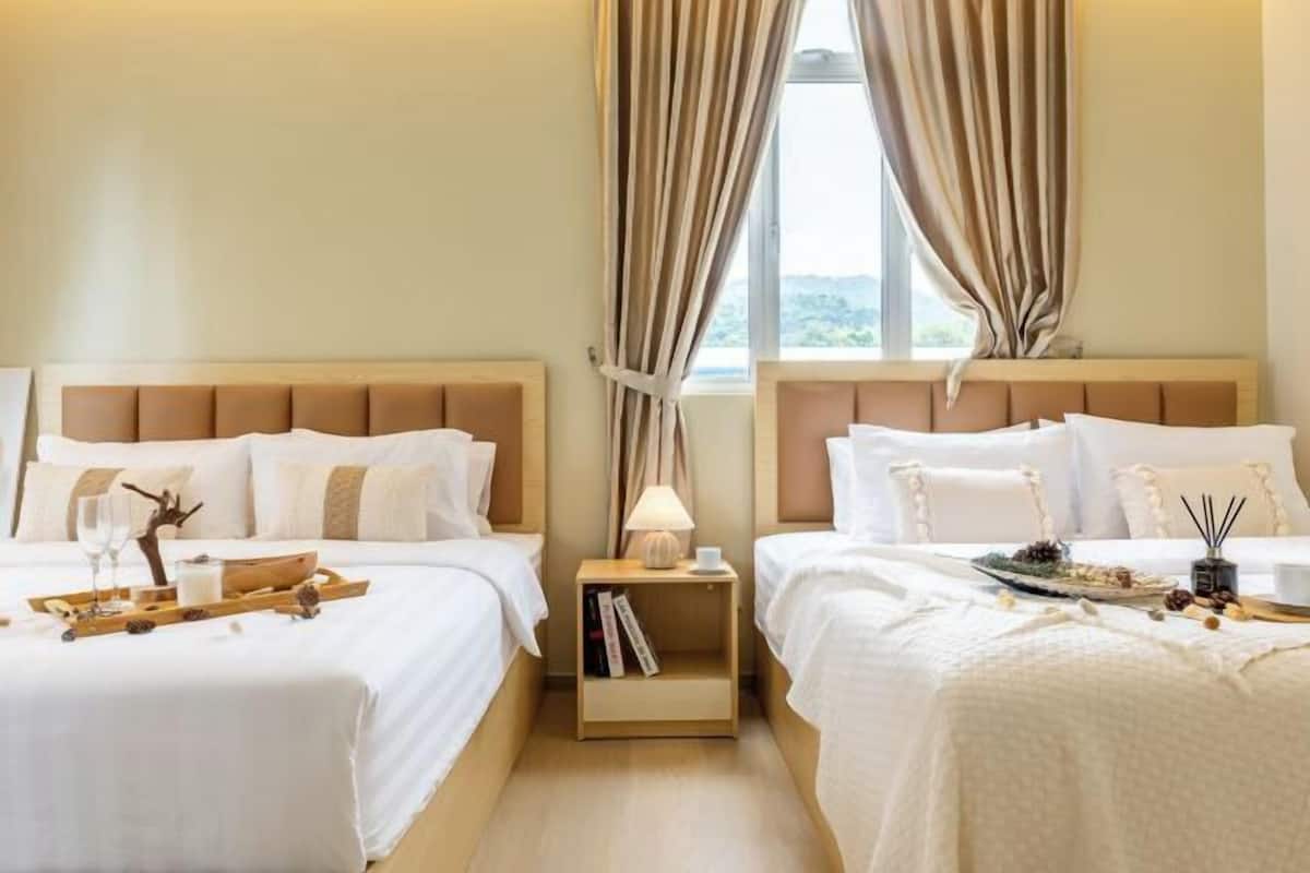 Ein Hotelzimmer mit zwei Betten, einem Nachttisch mit Lampe, einem Tablett mit Gläsern und einem Buch sowie einem Fenster mit Vorhängen.