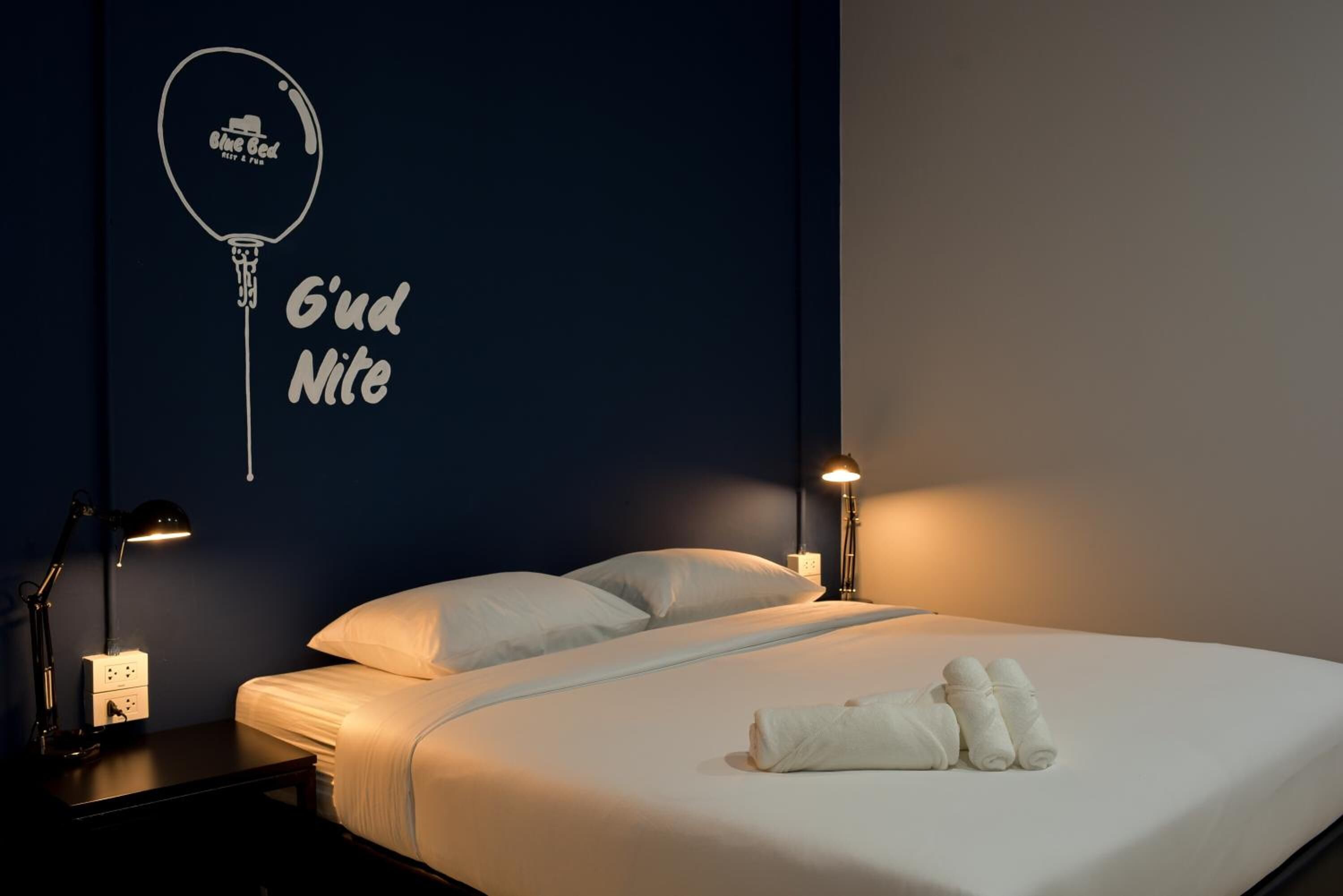 Una habitación de hotel con una cama, dos lámparas de noche, una mesita de noche y un adorno en la pared.