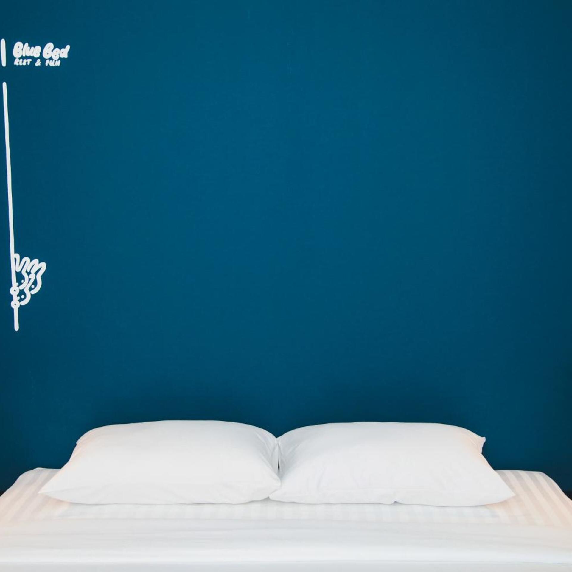 A bed with white bedding against a blue wall, a white sign with text, and a white decorative element.