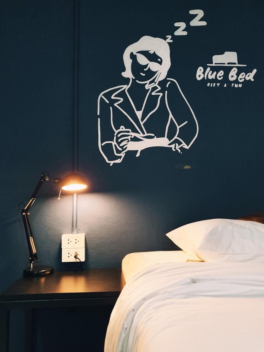 A bedroom with a wall decal of a person sleeping, a bedside lamp, and a bed with white bedding.