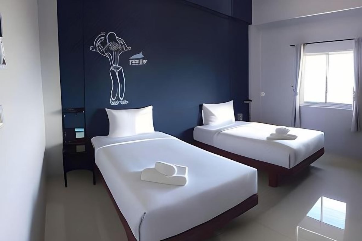 A hotel room with two beds, a dark accent wall, and a window.
