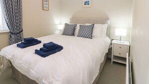 Una cama bien hecha con ropa blanca y toallas azules, una mesita de noche con lámpara y un cuadro en la pared.